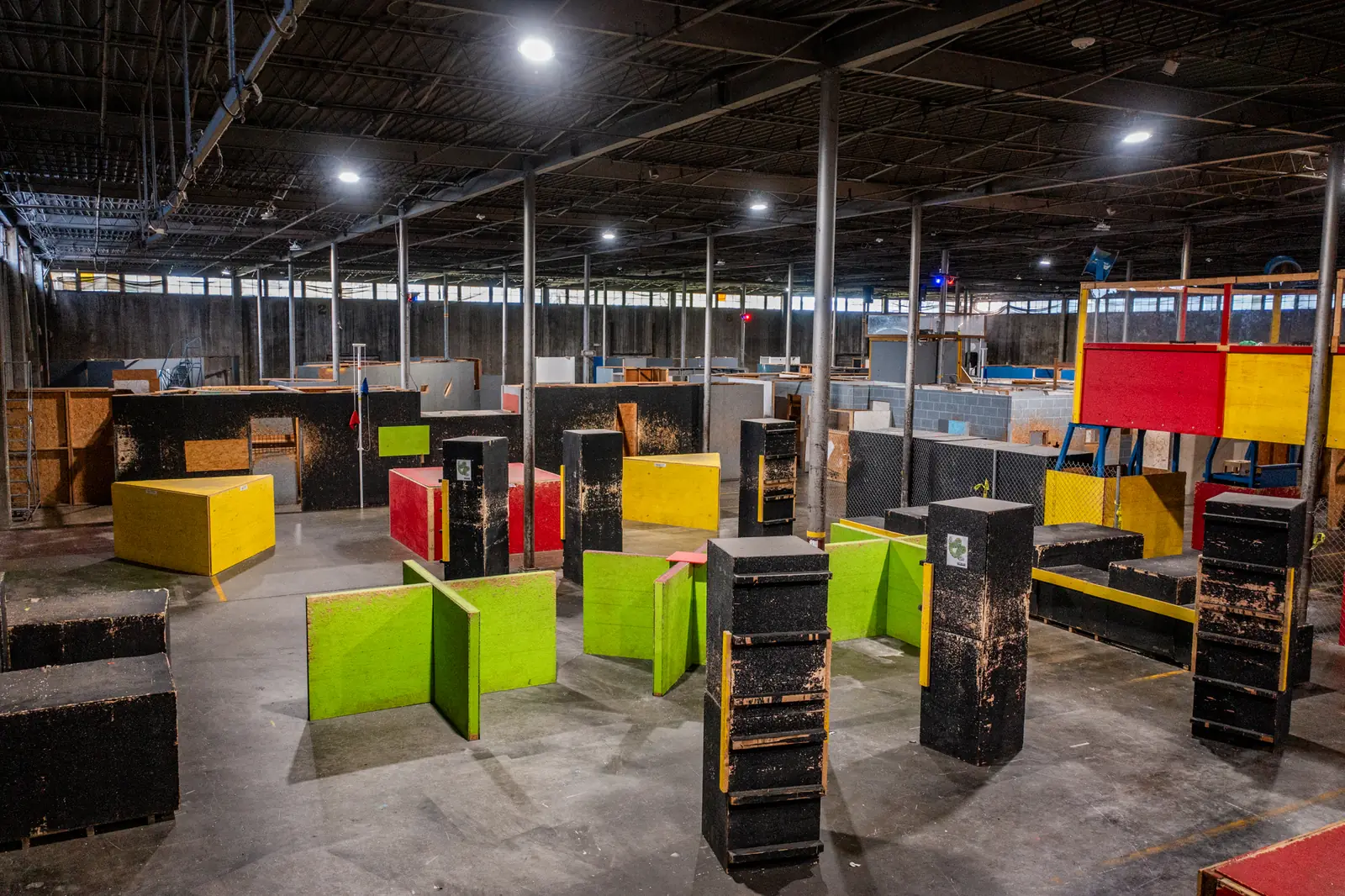 The Battalion arena floor: yellow, lime and black barricades under a high warehouse ceiling