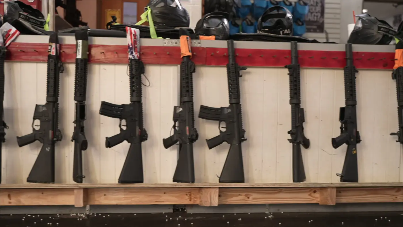 A row of rental rifles on a red-topped rack with masks above